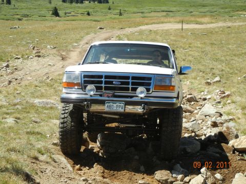 1996 Ford Bronco - White 1996 Ford Bronco driving off-road on a sunny day.