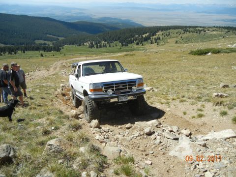 1996 Ford Bronco - A white Ford F-150 truck is driven off-road on a mountain trail with several people and a dog nearby.
