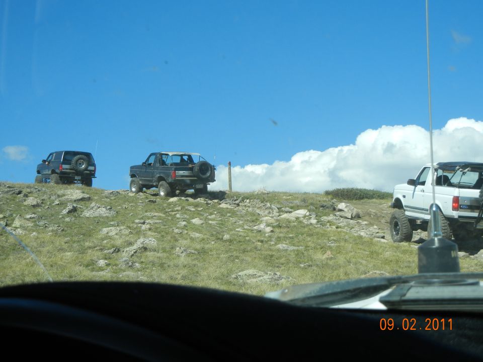 Three SUVs on a rocky hill; one black, one dark gray, one white. The dark gray SUV is a 1992-1996 Ford Bronco