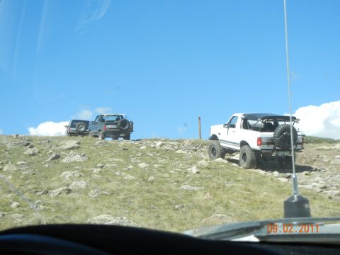 1996 Ford Bronco - Two SUVs, one a 1996 Ford Bronco, are parked on a rocky hill on a sunny day.