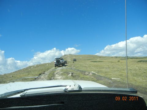 1996 Ford Bronco - Multiple SUVs navigate a challenging off-road trail on a sunny day with scattered clouds.