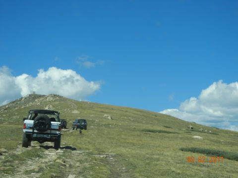 1996 Ford Bronco - A 1996 Ford Bronco navigates a rocky mountain trail under a bright blue sky, with another SUV following.