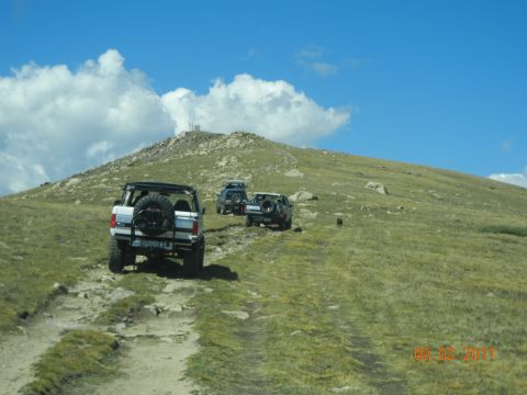 1996 Ford Bronco - A convoy of off-road vehicles navigates a challenging mountain trail on a clear day.