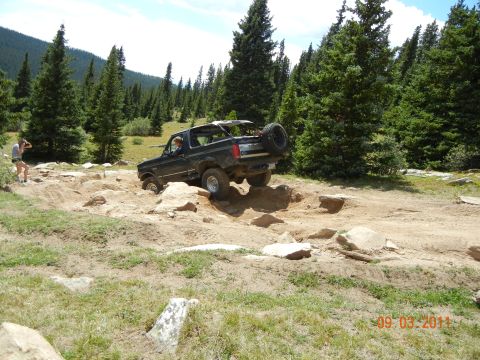 1996 Ford Bronco - A black Ford Bronco tackles a challenging off-road course with a person observing.
