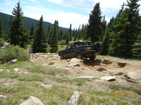 1996 Ford Bronco - A 1996 Ford Bronco tackles a challenging rocky off-road course surrounded by pine trees.