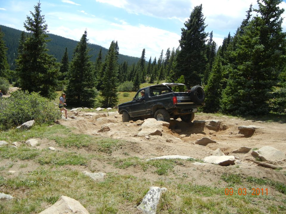 Dark 1996 Ford Bronco on rocky trail, rear-mounted spare tire visible