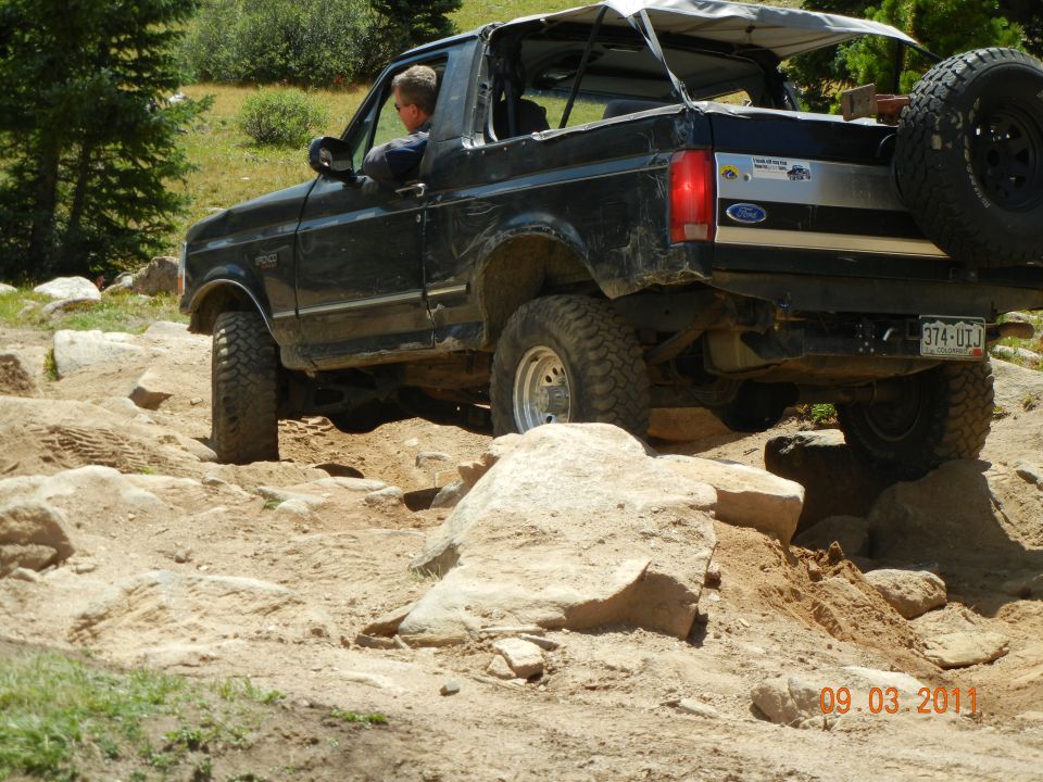 1996 Ford Bronco navigating a rocky trail, driver visible, spare tire mounted on rear