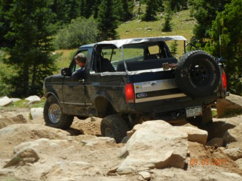 1996 Ford Bronco - This Ford Bronco is shown off-roading on a rocky trail with trees in the background.
