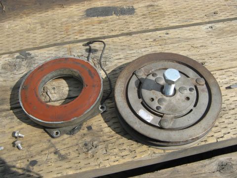 1972 Ford F-250 - Two parts of an air conditioning compressor clutch lie on a weathered wooden surface.