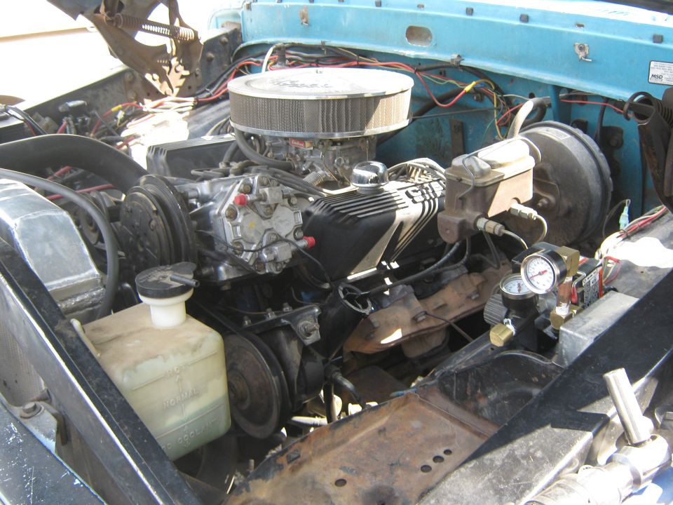 Engine bay of a light blue truck, showing a V8 engine with aftermarket air cleaner and chrome valve covers