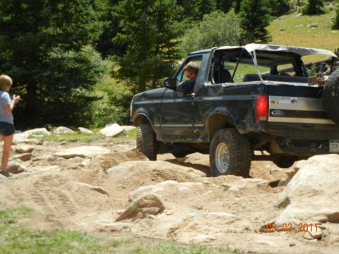 1996 Ford Bronco - A black 1996 Ford Bronco convertible navigates a challenging rocky terrain during an off-road excursion.
