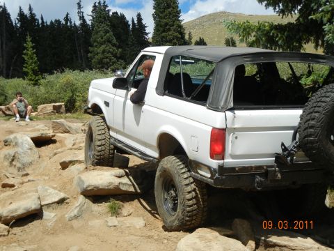 1996 Ford Bronco - 1996 Ford Bronco tackling a challenging rocky trail with a person sitting nearby.