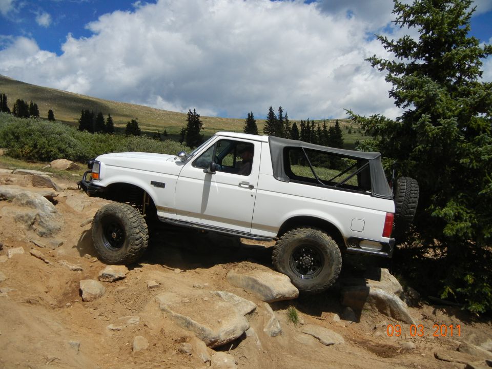 White 1996 Ford Bronco with a soft top navigating rocky terrain on a mountain trail