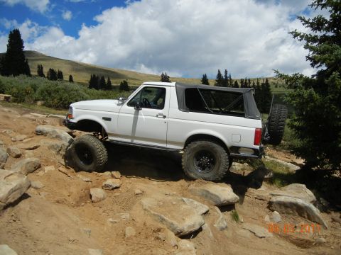 1996 Ford Bronco - This modified 1992 Ford Bronco tackles a challenging rocky terrain under a partly cloudy sky.