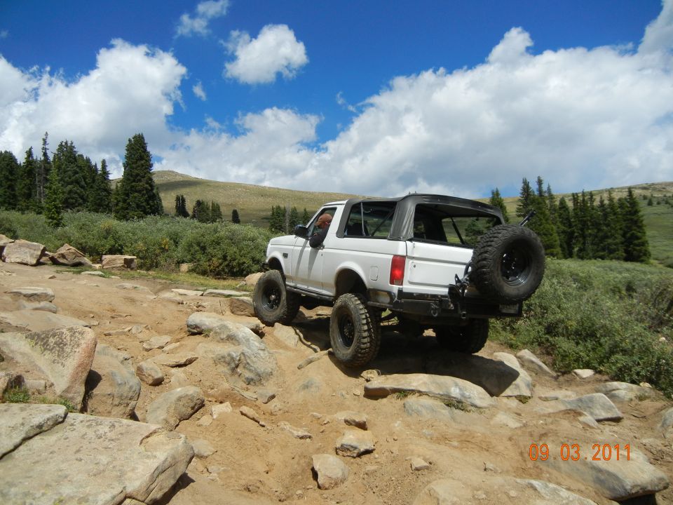 White 1996 Ford Bronco with a soft top, off-roading on a rocky trail