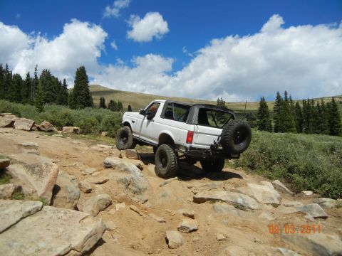 1996 Ford Bronco - A white 1990s Ford Bronco navigates a challenging rocky terrain under a bright blue sky.