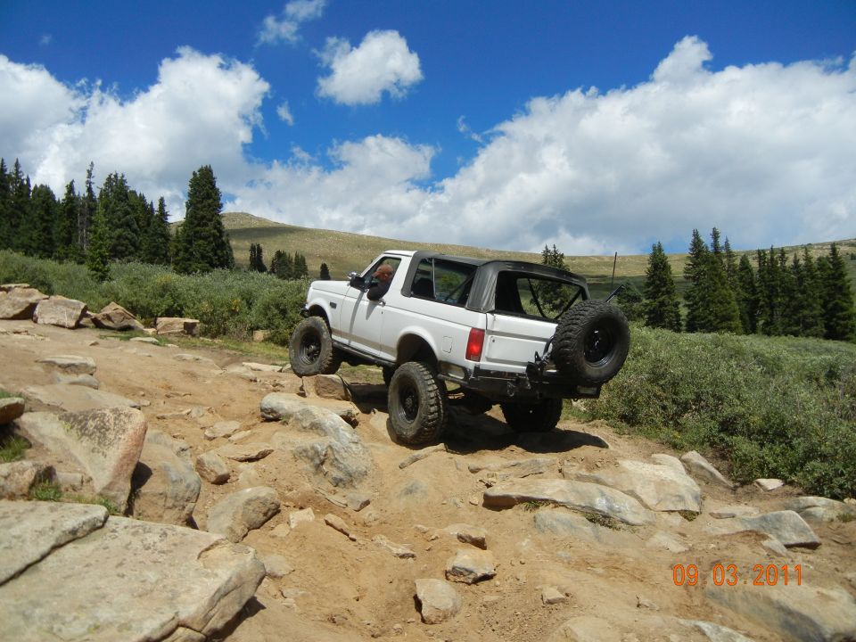 White 1990s Ford Bronco climbing rocks on a mountain trail