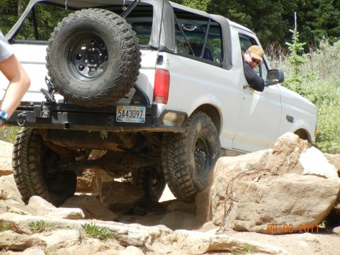 1996 Ford Bronco - A white 1996 Ford Bronco is shown off-roading over large rocks on a trail.