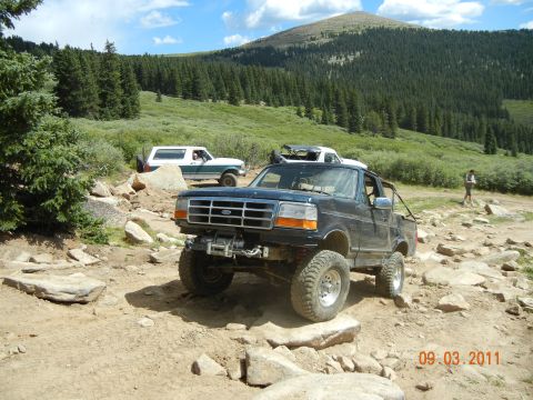1996 Ford Bronco - Multiple off-road vehicles navigate a rocky mountain trail on a sunny day.