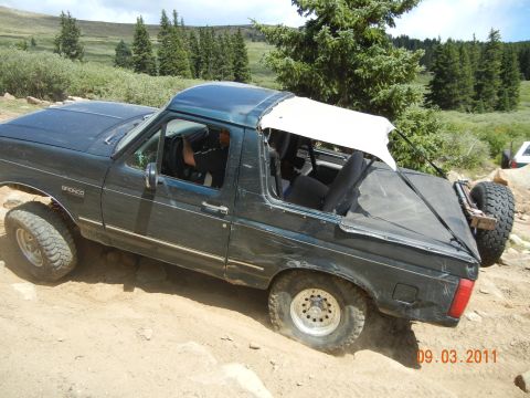 1996 Ford Bronco - This 1996 Ford Bronco navigates a rocky trail with its top removed, revealing the interior and spare tire mounted at the rear.