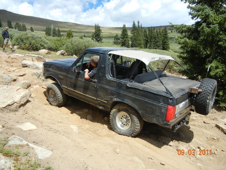 Black 1996 Ford Bronco with soft top on a rocky mountain trail, driver visible