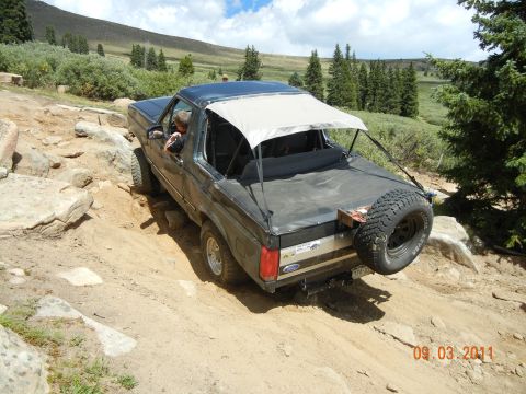 1996 Ford Bronco - A Ford Bronco tackles a challenging rocky path on a sunny day, with a spare tire mounted at the rear.
