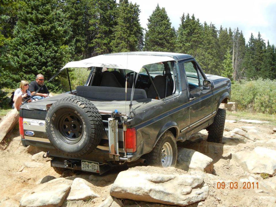 Ford Bronco navigating rocky terrain, spare tire on back, people in front