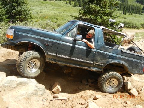 1996 Ford Bronco - Driver maneuvers a 1996 Ford Bronco over a challenging rocky terrain on an off-road trail.