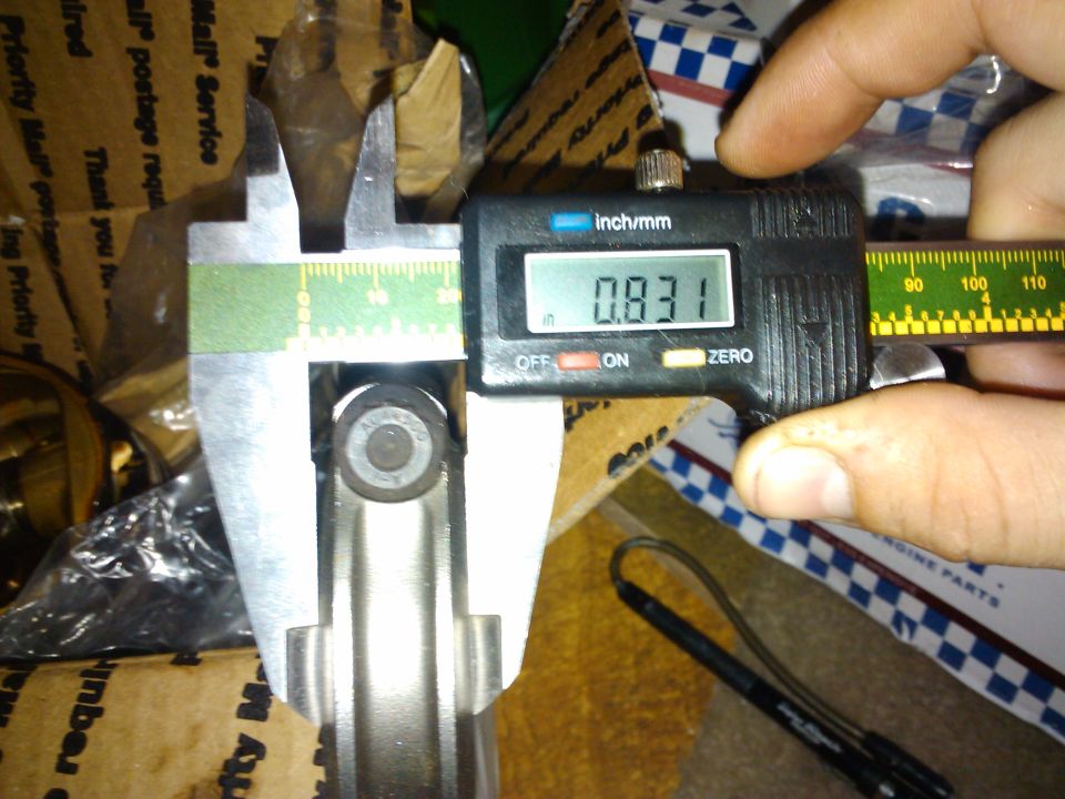 Digital calipers measuring a metal rod, reading 0.831 inches. Cardboard boxes in background
