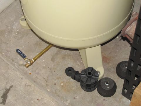 1993 Ford F-250 - Close-up of an air compressor tank's drain valve and several rubber mounting components on a concrete floor.