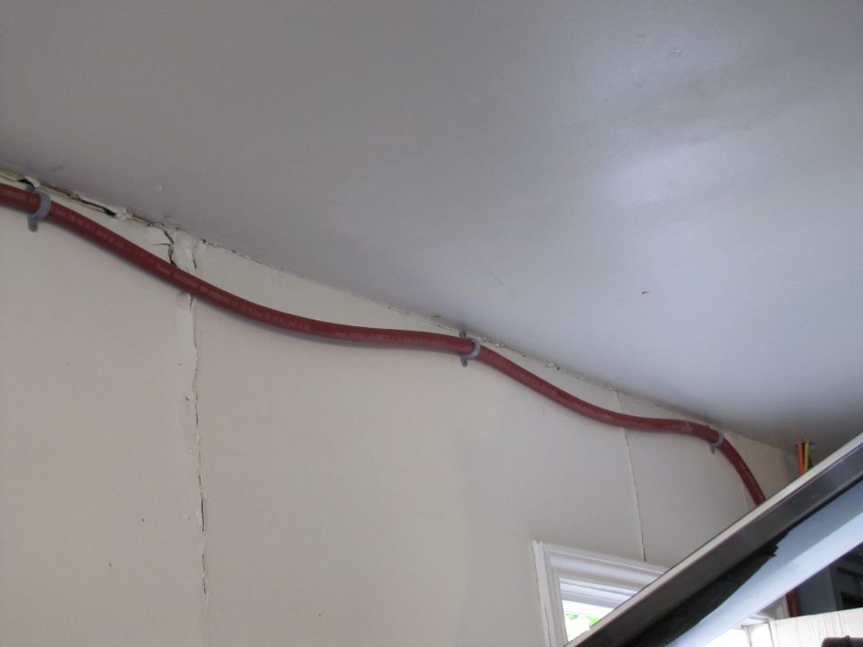 Red conduit secured with zip ties to a white ceiling and wall junction
