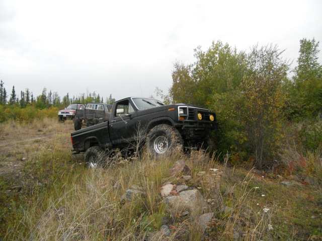 Black pickup truck with large tires on rocky terrain, other trucks in background