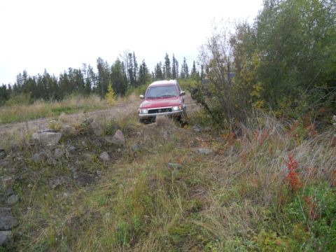 1986 Ford F-150 - A red SUV navigates a challenging dirt path through a wooded area.