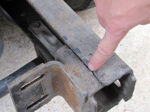 1993 Ford F-250 - A finger points to a crack in the metal frame of a vehicle, indicating damage.