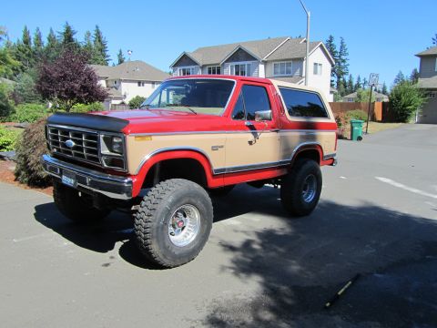 1984 Ford Bronco - Lifted 1984 Ford Bronco with two-tone red and tan paint parked on a paved surface.