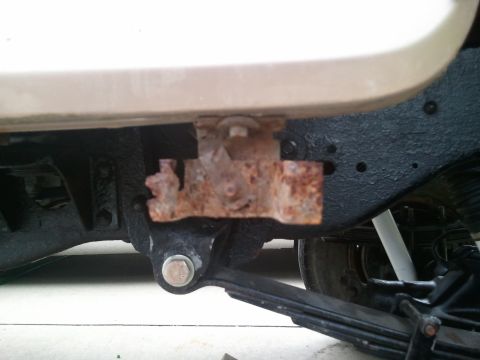 1996 Ford Bronco - A heavily rusted bracket is attached to the underside of a vehicle's frame, showing signs of wear and tear.