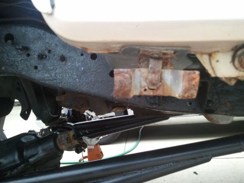 1996 Ford Bronco - Close-up view of the rusted frame and suspension system of a vehicle, showing mechanical components and an orange jack.