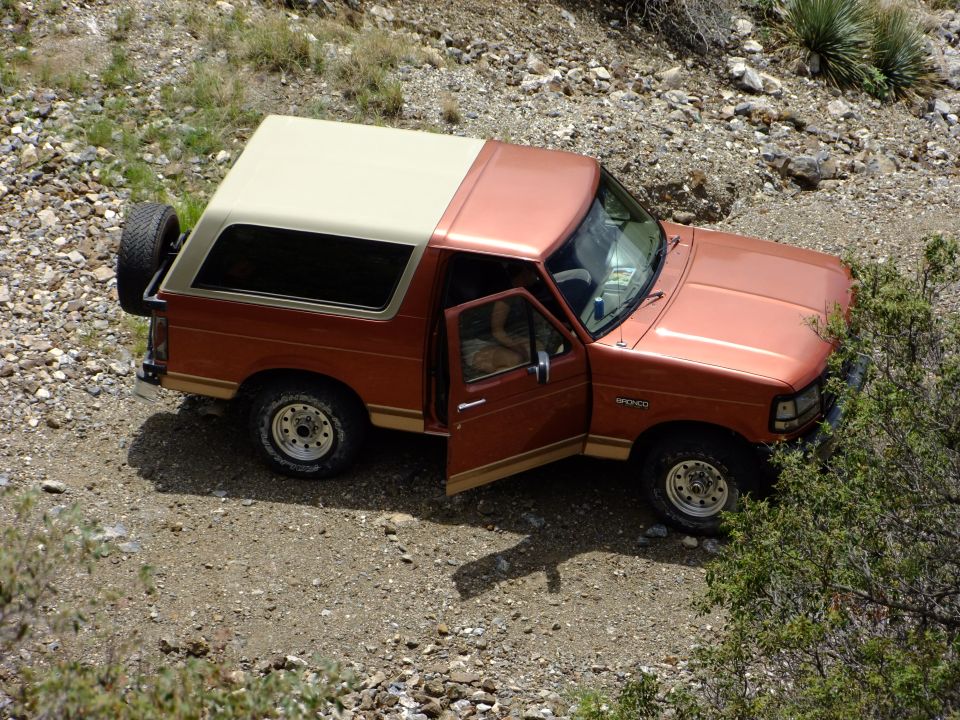 Orange Ford Bronco parked on a dirt road with the driver's door open