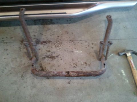 1996 Ford Bronco - A rusty step bar lies on a concrete floor next to a hammer, with part of a vehicle's side visible above.
