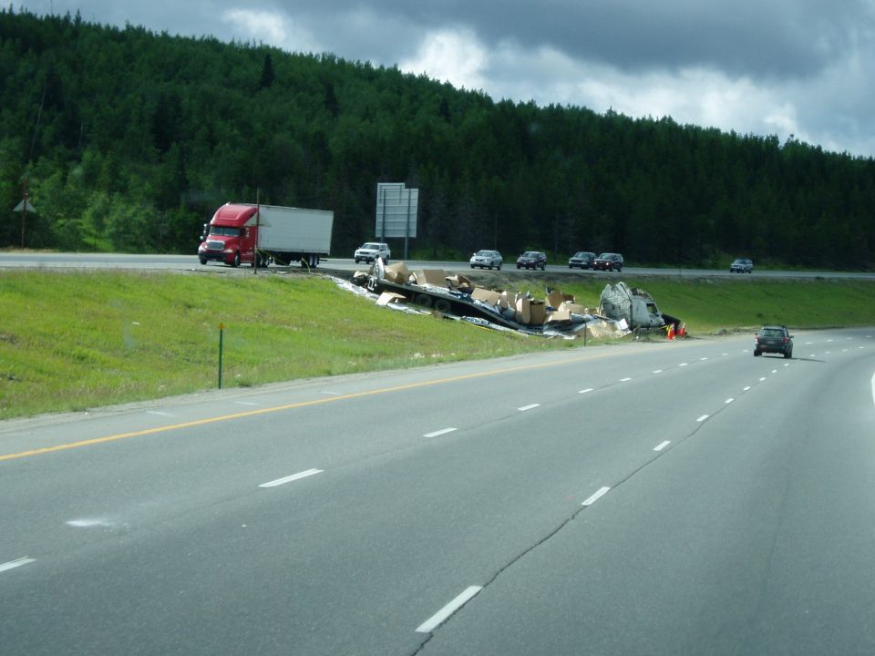 Red semi-truck on highway next to overturned trailer spilling cargo