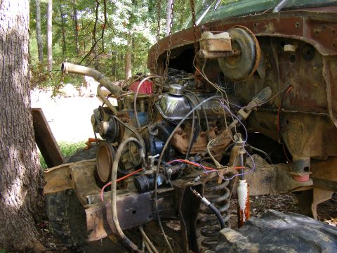 1978 Ford Bronco - The engine bay and front suspension of a heavily weathered vehicle are visible, with parts hanging from chains.