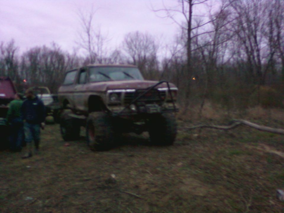 Red 1978 Ford Bronco with a brush guard and large tires, parked in a muddy, wooded area