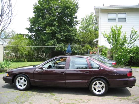 maroon sedan parked next to another car in a suburban driveway with trees and a house in the background