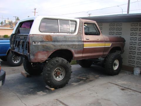 1979 Ford Bronco - This heavily modified Ford Bronco features oversized tires and a lifted suspension, with visible rust and missing rear bodywork.