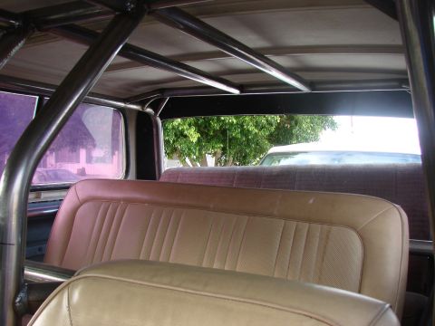 1979 Ford Bronco - The interior of a vehicle shows tan seats and a metal roll cage structure overhead and another vehicle outside.