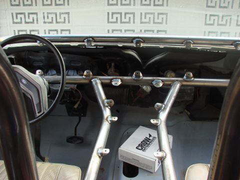 1979 Ford Bronco - The interior of a vehicle features a custom roll cage, a steering wheel, and a box of parts on the passenger side.