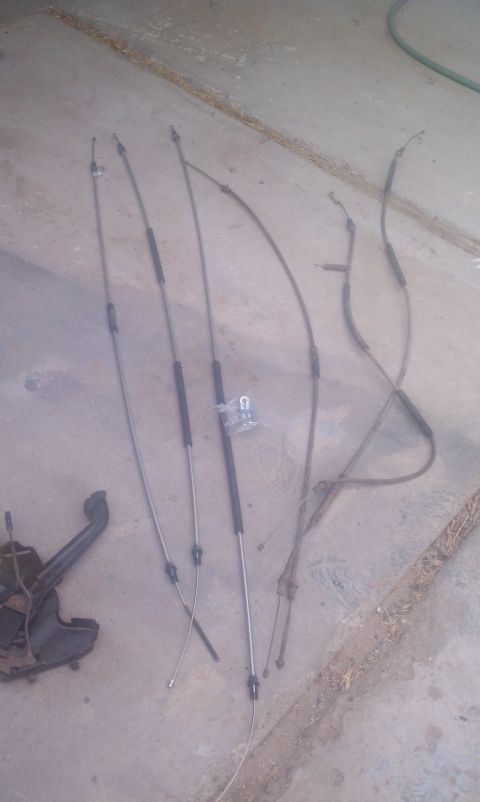 1979 Ford Bronco - Parking brake cables and a bracket are laid out on a concrete surface.