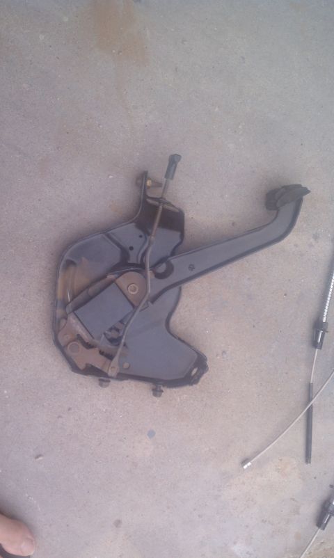1979 Ford Bronco - A parking brake assembly and cable are shown lying on a concrete surface.