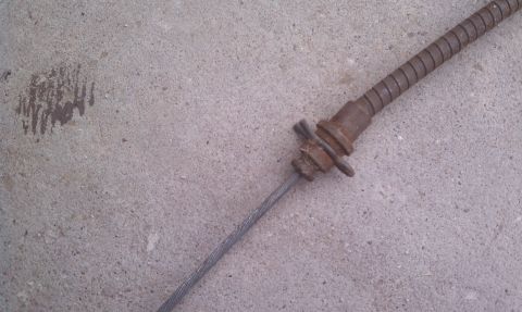 1979 Ford Bronco - A close-up view of a rusty parking brake cable and its protective sheath rests on a concrete surface.