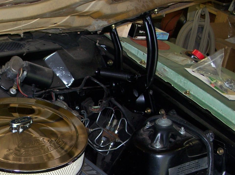 Hood hinge and spring in an engine bay next to a wiper motor and chrome Ford Racing air cleaner